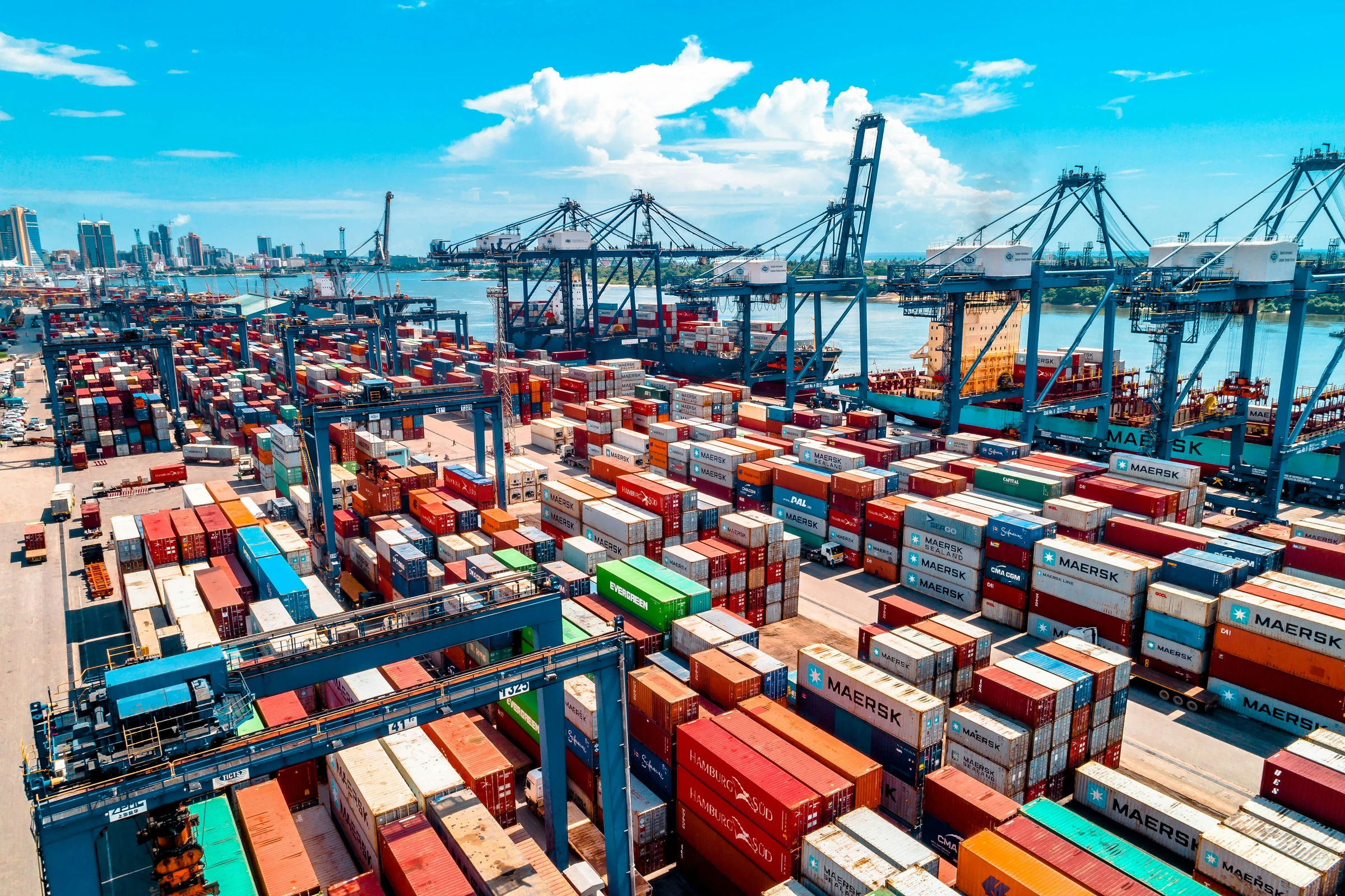 A tall stack of multicoloured shipping containers in a working port, photographed from below against an open sky.